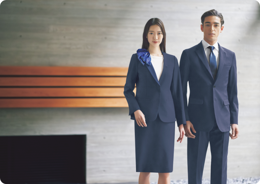 ENJOY Noirのネイビー色の制服を着用し、ホテルのカウンター前に立つ男女スタッフ