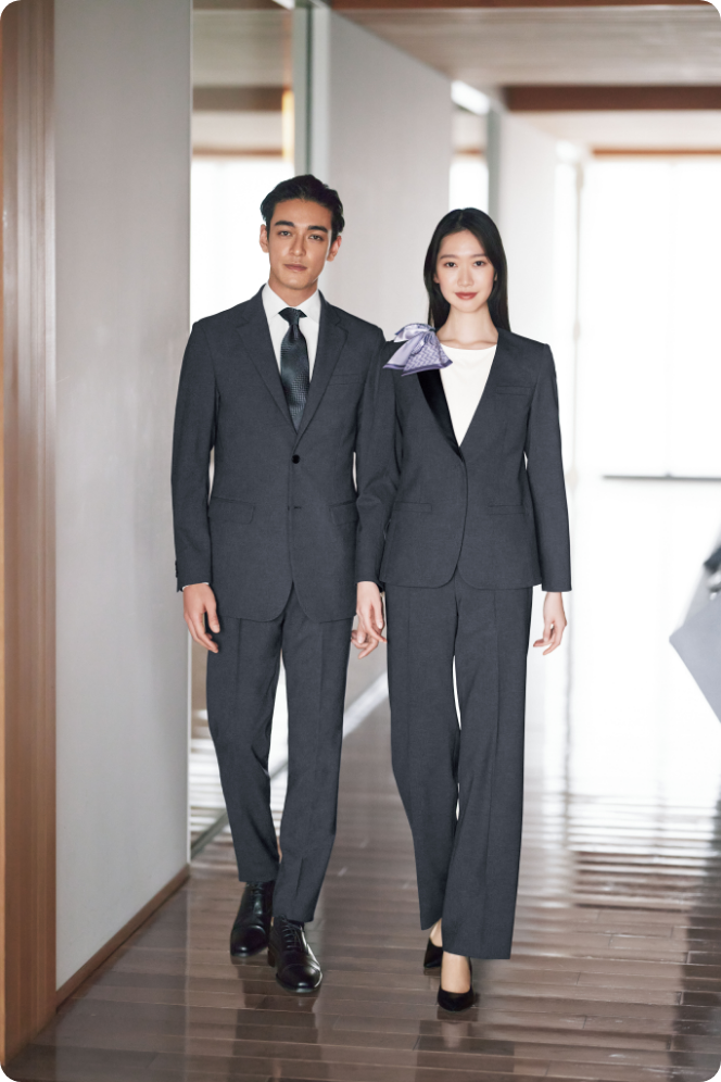 ENJOY Noirのグレー色の制服を着用し、ホテルの廊下を歩く男女スタッフ