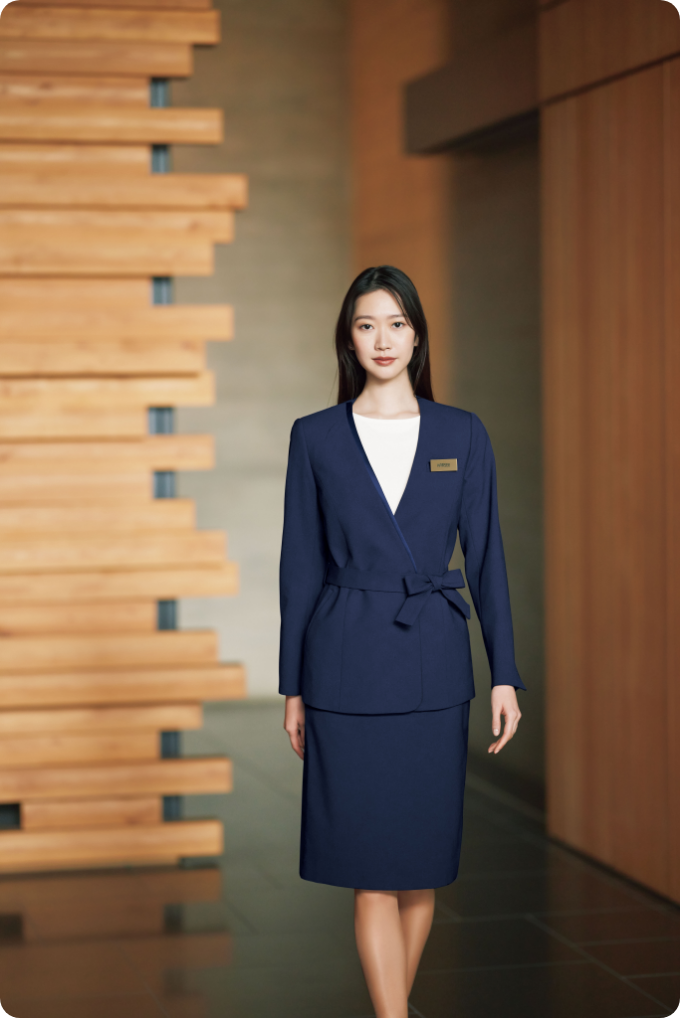ENJOY Noirのネイビー色の制服を着用し、ホテルの廊下を歩く女性スタッフ