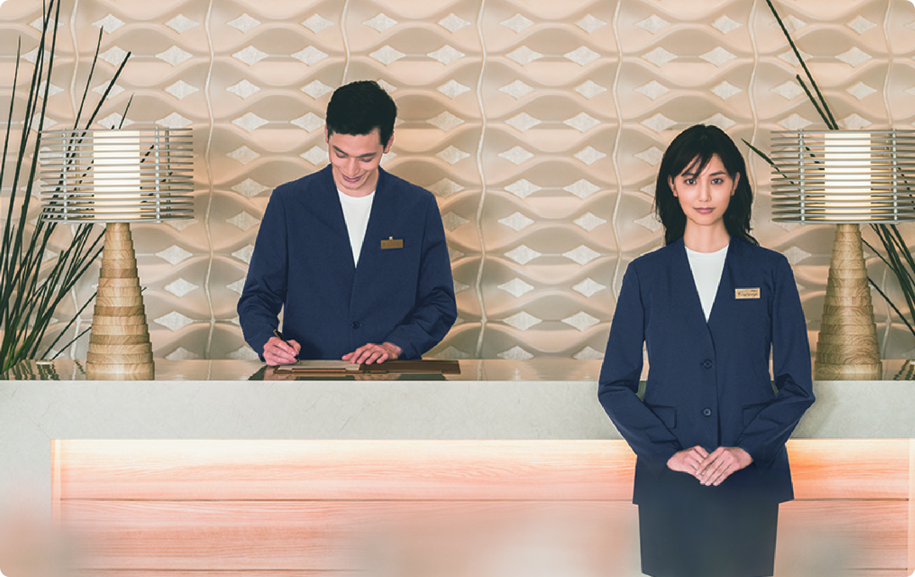 ENJOY Noirの黒色の制服を着用し、受付カウンターで業務を行う、上品で清潔感のあるレセプションスタッフ