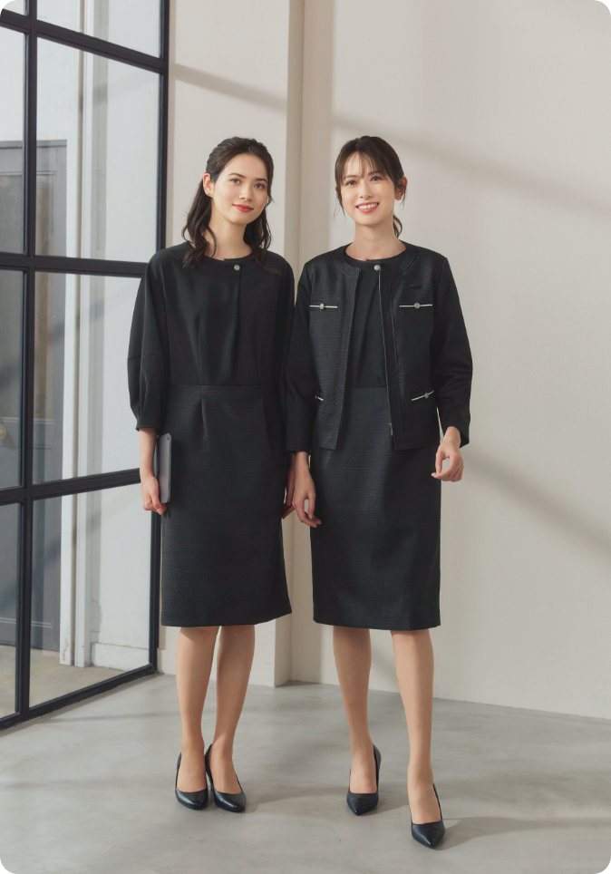 ENJOY Noirの黒色の制服を着用し、笑顔で立っている2名の女性レセプションスタッフ